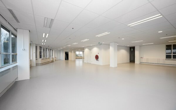 Ruime, lege kantoorruimte in Rivium Quadrant met witte muren, systeemplafond en grote ramen.